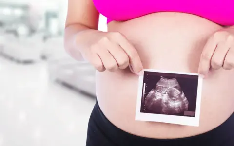 Ciężarna kobieta trzyma zdjęcie USG płodu na tle rozmazanego wnętrza.