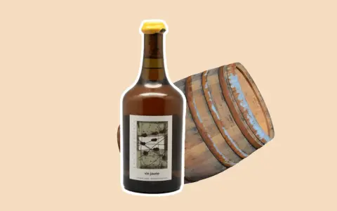 Bouteille de vin jaune à côté d'un vieux fût de chêne. Le vin jaune, une spécialité du Jura, est un vin oxydatif unique.