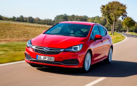 Czerwony Opel Astra jedzie po krętej drodze. W tle pola i drzewa. Idealny do diagnostyki z **op-com opel po polsku**.