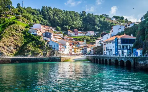 Un pintoresco pueblo costero con **5 villas** coloridas apiladas en una colina verde, frente a un mar turquesa.