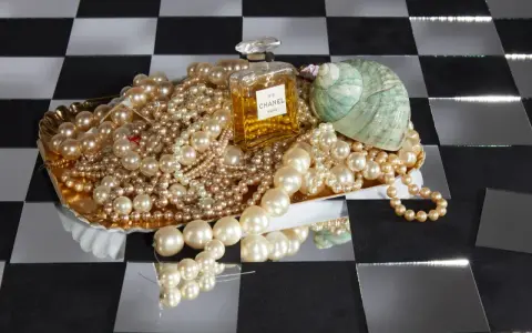 Perle, profumo Chanel N°5 e una conchiglia su un vassoio dorato. Il profumo evoca il **chanel significato** di lusso e raffinatezza.