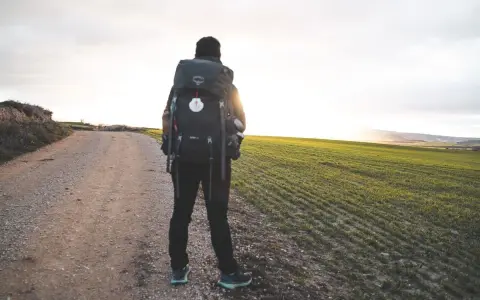 Pellegrino solitario su un sentiero sterrato, con un campo verde a destra. Le sue cammino di Santiago esperienze negative sono un ricordo lontano, mentre il sole tramonta.