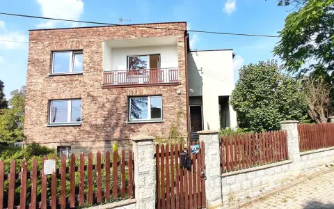 Nowoczesna metamorfoza domu z lat 80. z ceglaną fasadą, balkonem i drewnianym płotem.