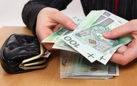 Dłonie liczą banknoty 100 zł obok portmonetki. Zastanawiasz się, ile wynosi trzynasta emerytura netto?