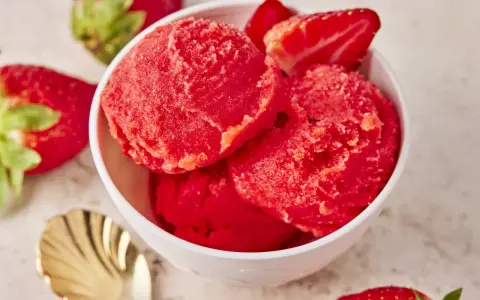 Schüssel mit erfrischendem Erdbeer Sorbet, garniert mit frischen Erdbeeren und einer goldenen Löffel.