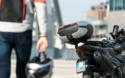 Un motociclista con casco in mano si avvicina alla sua moto. Andare in moto fa bene, un'avventura ti aspetta!