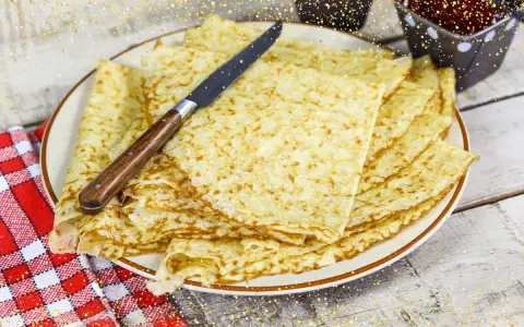Pile de crêpes bretonnes dorées sur une assiette, prêtes à être dégustées. Un couteau est posé dessus.