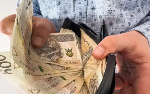 Ręce wkładają banknoty 200 zł do portfela. To może być nagroda jubileuszowa za długoletnią pracę.