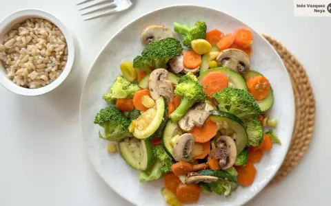 Un colorido salteado de verduras con brócoli, zanahoria, calabacín y champiñones, servido junto a un tazón de arroz integral.