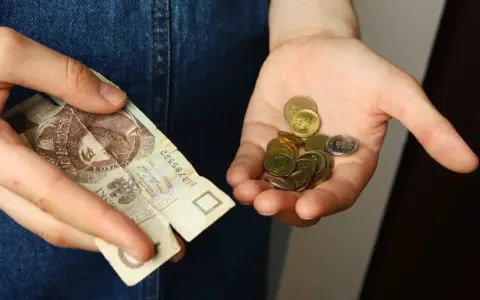 Dłoń trzyma banknot 20 zł i garść monet. Symbolizuje to spłatę długu po wyroku sądowym, gdzie każda złotówka ma znaczenie.