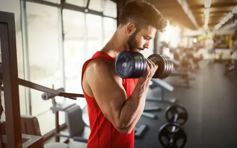 Hombre con barba entrenando bíceps con mancuerna en gimnasio. ¿Cuál es la mejor hora para entrenar?