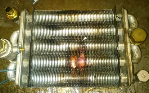 Scambiatore caldaia con evidenti segni di bruciatura, causa rottura scambiatore caldaia. Componenti metallici corrosi e deformati.