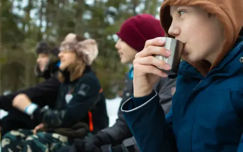 Barn njuter av fika under friluftsdag aktiviteter i snöig skog. En pojke dricker ur en metallmugg.