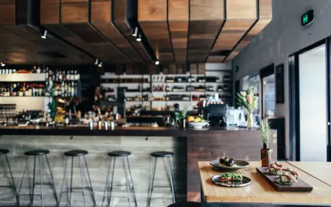 Ambiente restaurante moderno con barra, taburetes y aperitivos en mesa.