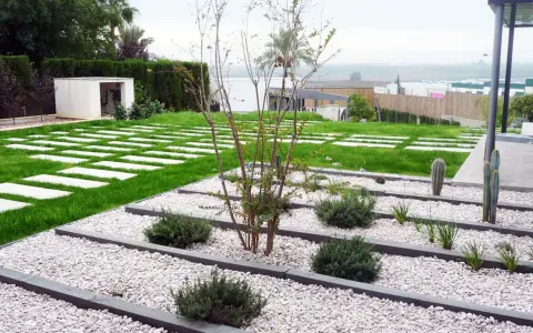Vialetti giardino moderni con lastre quadrate su prato verde e aiuole di ghiaia bianca con piante succulente e arbusti.