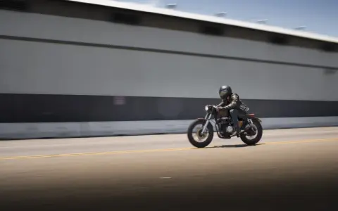 Motociclista con casco y chaqueta de cuero sobre una moto estilo cafe racer, en movimiento rápido por una carretera. El carmet a2 es su compañero de aventuras.