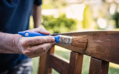 Mano aplicando barniz a un banco de jardín, creando un hermoso efecto madera.