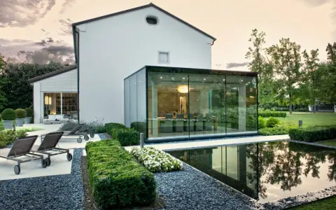 Ampliamento casa con estensione esterna in vetro, con piscina e arredi da giardino.