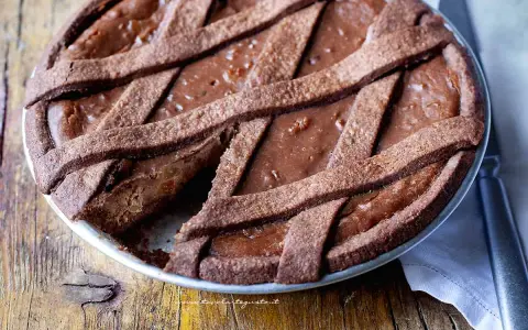 Pastiera al cioccolato con scorze candite, un dolce goloso su un tavolo di legno rustico.