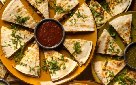 Pyszna quesadilla z mięsem mielonym, pokrojona w trójkąty, podana z salsą i zielonym sosem.