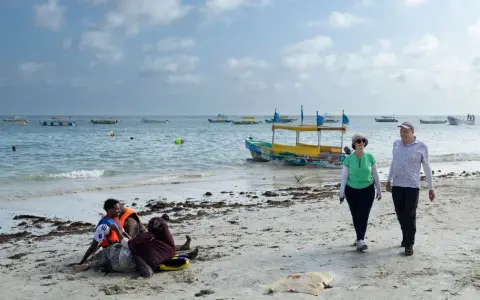 Spacerowery na plaży w Somalii, z łodziami na morzu. Czy Somalia jest bezpieczna? Turyści spacerują, podczas gdy lokalni mieszkańcy odpoczywają na piasku.