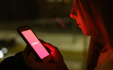 Dziewczyna patrzy na ekran telefonu z logo Tindera. Zastanawia się, co odpisać na "czego szukasz na Tinderze?".