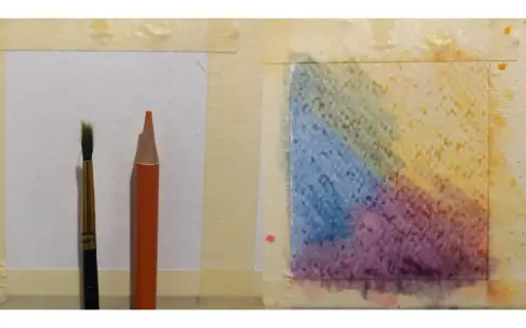 Un pinceau et un crayon aquarelle orange sont prêts pour l'utilisation. Une zone de papier présente des dégradés de couleurs vives.