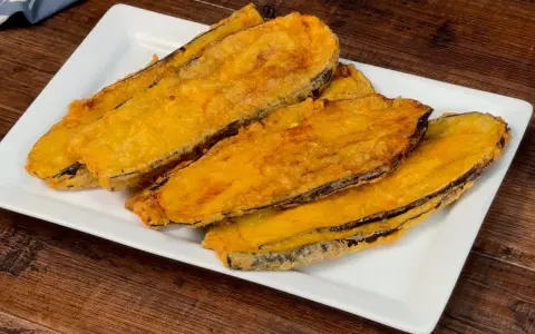 Fette di melanzane fritte, dorate e croccanti, servite su un piatto bianco. Un assaggio delle deliziose melanzane alla pullastiello.