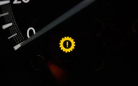 Gelbes Warnlicht mit einem Zahnrad und Ausrufezeichen im Auto-Armaturenbrett. Ein Zeichen für ein Problem mit dem Getriebe.
