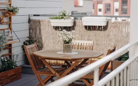 Holztisch mit Stühlen und Gänseblümchen, Wandregal mit Pflanzen, schöne Balkon Ideen für Ihr Zuhause.