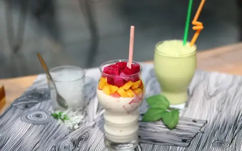 Pyszny koktajl białkowy z kawałkami smoczego owocu i mango. Obok zielony smoothie i szklanka z lodem.