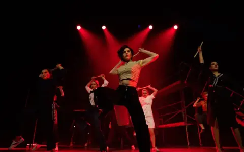 Grupa tancerek na scenie, w rytm muzyki, z pałeczkami w dłoniach. To właśnie co to jest rap – energia i ekspresja.