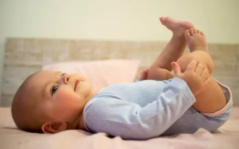 5-miesięczne dziecko leży na plecach, podnosząc nóżki i bawiąc się nimi. To pokazuje, co potrafi 5 miesięczne dziecko.