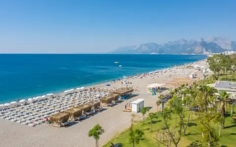 Piękna plaża z rzędami leżaków i parasoli, gdzie jest Antalya. Błękitne morze i góry w tle tworzą idealny krajobraz.