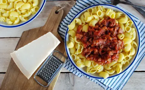 Makaron z sosem mięsnym, kawałek parmezanu i tarka na desce.