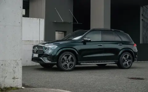 Elegancki, ciemnozielony Mercedes GLE 2025 zaparkowany przed nowoczesnym budynkiem.