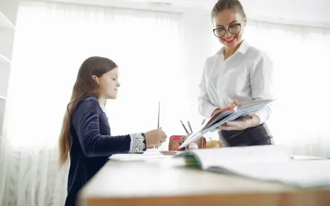 Nauczycielka pomaga dziecku z dysleksją w szkole, cierpliwie tłumacząc materiał z książki.