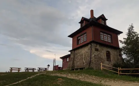 Drewniana wieża widokowa na Luboniu Wielkim, z kamiennym fundamentem, otoczona zielenią i ławkami.