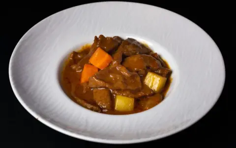 Un delicioso estofado de ternera con trozos de zanahoria y patata en una salsa espesa y aromática, servido en un plato blanco.