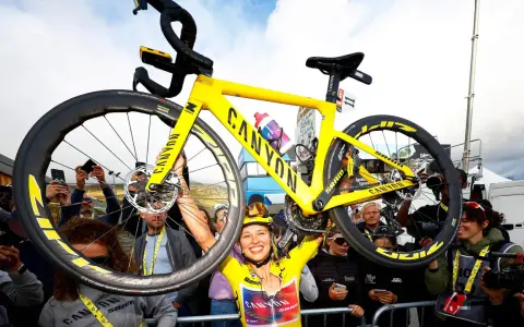 Jubelnde Radfahrerin hebt ihr gelbes Canyon-Rennrad hoch. Ein Moment des Triumphs bei der Frauen Tour de France.