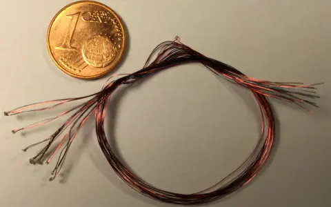 Ein-Cent-Münze neben einem Bündel dünner roter und schwarzer Kabel mit kleinen Lötpunkten.