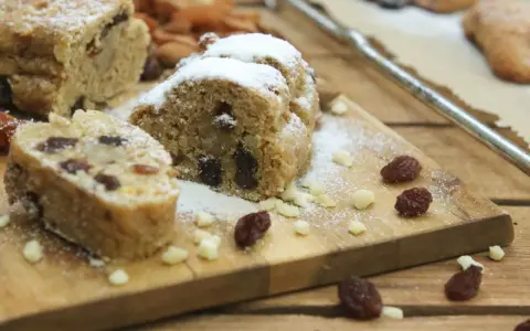 Stollen formen ohne backform: saftige Stollenstücke mit Rosinen und Puderzucker auf Holzbrett, umgeben von Nüssen und Trockenfrüchten.