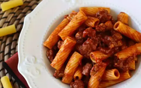 En portion pasta med korv i tomatsås, serverad på en vit tallrik.