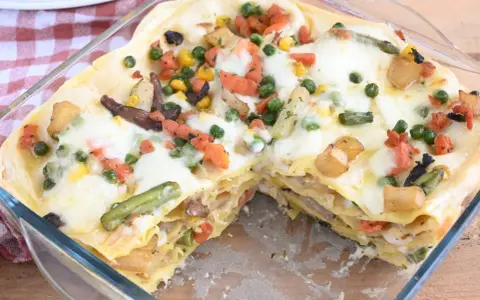 Lasagne di verdure dorate e filanti, con piselli, carote, patate e fagiolini, in una teglia di vetro.
