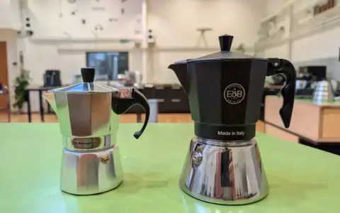 Zwei Espressokocher, ein silberner und ein schwarzer, stehen bereit für den perfekten Espresso auf dem Herd.