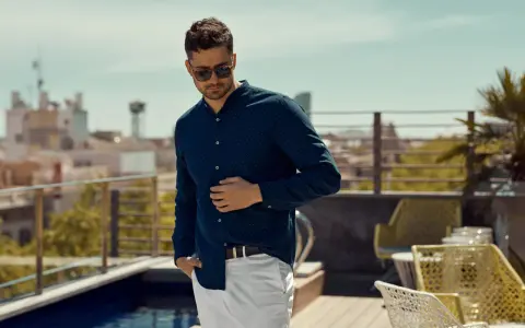 Mężczyzna w granatowej koszuli w kropki i białych spodniach, prezentujący luźny elegancki styl męski na tarasie z widokiem na miasto.