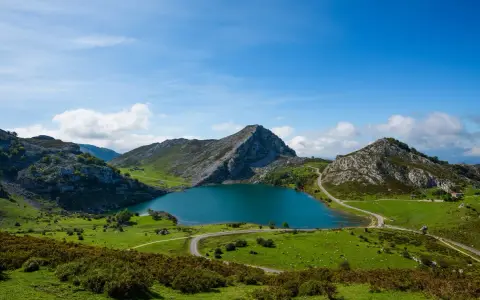 Lago azul rodeado de montañas verdes y caminos sinuosos, parte de la red de parques nacionales.
