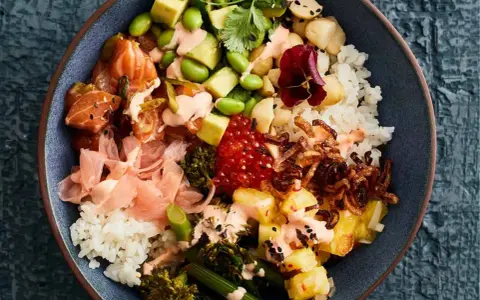 Eine bunte Poke Bowl mit Lachs, Avocado, Edamame, Reis, eingelegtem Ingwer und knusprigen Zwiebeln.