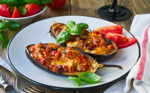 Melanzane ripiene senza carne, dorate e filanti, guarnite con basilico fresco e pomodoro. Un piatto vegetariano invitante.