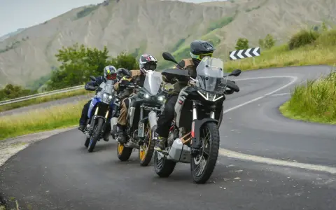 Quattro motociclisti in fila su una strada tortuosa tra colline verdi. Sei motociclista se ami l'avventura.